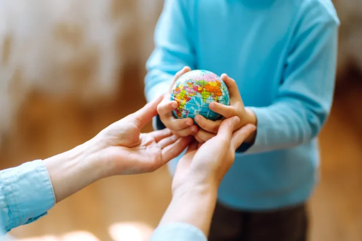 Manos de una persona adulta y un niño sosteniendo juntos un globo terráqueo