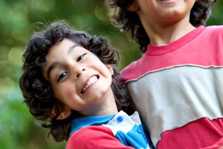 Dos niños sonriendo y abrazados al aire libre